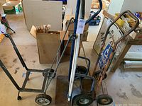 Photo showing three hand trucks of various sizes next to each other, two black handled and one rusted small hand truck.