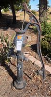 Full view of vintage wrought iron water pump outdoors showing handle and base.