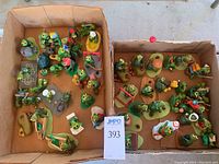 Top-down view of two boxes containing over 30 small green turtle figurines engaged in different activities, showing variety and group arrangement.
