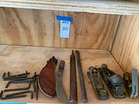 Photo of the skinning blade, leather sheath, Allen wrenches, two metal files, metal wedge, and two metal hand planers all placed on wooden surface.