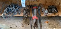 View displaying multiple farm-related metal items on a wooden shelf including chains, manual crank pulley devices, wrought iron door straps, and a trailer hitch ball mount.
