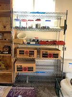 Full view of chrome wire shelving unit containing various boxed items and plastic containers on shelves, showing overall condition and size.