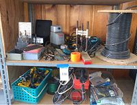 Shelf showing assortment of drill bits, parts, wiring, two drills, and electrical fencing controller.