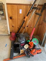 Photo showing multiple garden tools including Black & Decker hedge trimmer, red Power Sweep leaf blower, Toro and Eco weedwhackers, 1 gallon shop vac, and various accessories like line spools and battery charger.