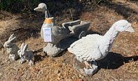 Full view of four outdoor garden statues on dirt ground showing all geese and rabbits.