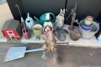 All items together showing variety: metal windmill top, watering cans, galvanized pots, wooden barn birdhouse, large bells, decorative water pumps, and planters