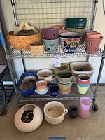 Full view of metal shelving with multiple sizes and styles of pots and planters including colorful Mexican pot and large orange conch shell style pot