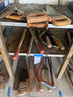 Multiple hand tools including loppers with wooden handles, detached saw handles, and pruning trimmers on a metal shelf.
