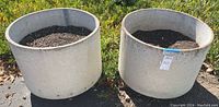 Two large concrete planters viewed from above filled with soil outdoors, showing round shape and light color
