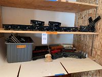 Shelf view showing multiple black B&O coal hopper cars on top shelf, assorted dozen train cars including a black steam locomotive and freight cars on bottom shelf, plastic bin of train track pieces.