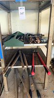 Shelf with green toolbox holding assorted pulley hooks and metal tools, two hammers next to it, and four loppers with wooden and red handles.
