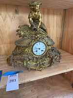 Front view of ornate metal mantle clock with farmer figurine tying wheat sheafs showing clock face and detailed floral scrollwork.