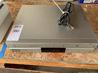 Front full view showing top and front panel of the silver Panasonic DVD and VHS player combo with power cord placed on top.