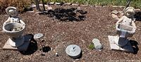 Wide view showing the boy and girl cement statues, metal sundial, and garden ground with mulch. Both statues are standing on flat pavers.