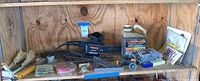 Wide view of shelf with Remington Limb n Trim tool, oil container, finish nails, staple fasteners, steel wool, miscellaneous parts, and tools.