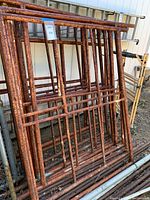 Stack of about 12 rusty metal grid scaffolding pieces with rectangular bar design, showing heavy rust on surface.