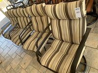 Front view of four patio armchairs with gray and brown striped cushions and black metal swivel bases lined up in a row.