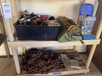 Bin on shelf with assorted hand tools and a tool bag next to it, large heavy chain on lower shelf