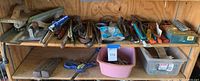 View of wooden shelving unit with assorted hand tools arranged on two shelves including wrenches, clamps, pliers, and bins of hardware.