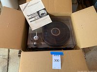 Turntable in cardboard box with transparent dust cover on and original manual placed on top