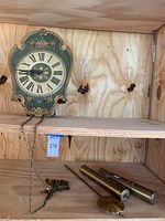 Painted wood wall clock on shelf with chains hanging and two brass weights and a pendulum below