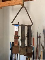 Photo showing three rusted metal cowbells attached to thick leather belts hanging on a wooden beam.