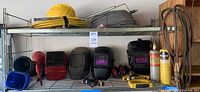 Photo showing the shelving unit holding all items including hard hat, welding helmets, funnels, ear covers, hoses, gauges, and gas cylinders.