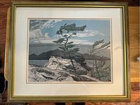 Full view of the framed print showing the artwork featuring pine trees on rocky cliffs with a lake and mountains in the background.