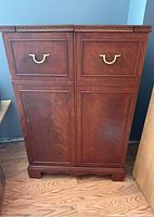 Front view of closed wooden bar cabinet with two drawers and brass handles.