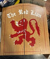Closed view of wooden cabinet with red lion artwork, front exterior of the dartboard cabinet.