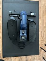 Top-down view of the blue elliptical bike on a black mat, showing two textured black pedals and the digital control display.