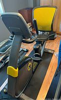 Side angle view of the Livestrong recumbent bike showing padded seat with backrest, pedal straps, and part of the exercise mat.