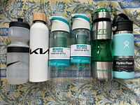Front view of 7 water bottles including Nike, KW, Style, Teva and Hydro Flask brands on a patterned cloth.