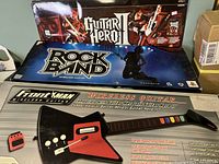 Four wireless guitar controllers, including one Guitar Hero II branded, with packaging visible, and a small red wireless accessory.