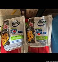 Two bags of Roundup Landscape Weed Preventer for garden use, displayed side by side on a red surface.