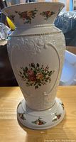 Front view of white ceramic vase embossed with floral and basket weave patterns with Old Country Roses floral decals and gold trim.