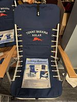 Front view of Tommy Bahama navy blue beach chair showing embroidered logo, wooden armrests, and attached product information sheet.