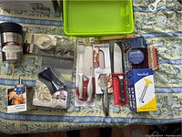 Overview photo of all kitchen gadgets and cutting tools laid out on patterned cloth including boxed items and loose items.
