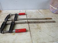 Two large bar clamps placed side by side showing total length and condition on topside facing up.