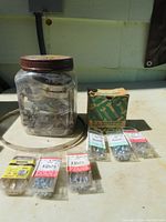 Jar with mixed metal clamps and small retail boxes of screws on a table outdoors