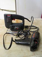 Front side view of the black Skil jigsaw tool with attached power cord on a wooden surface.