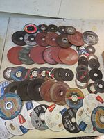 Various grinding discs laid out flat in mixed sizes and conditions, some heavily used, some new. Discs from multiple manufacturers visible.