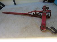 Side view of red metal ratchet come along laid on a table showing tool length and hook end.