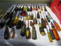 44 screwdrivers laid out on cloth showing various handle colors and materials with visible wear and some rust spots.