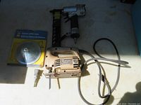 Full lot view showing Black & Decker jigsaw, new bearing packer package, and pneumatic nail gun tool
