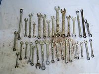 Overview of 34 used wrenches laid out in rows, showing different sizes and types including combination, open-end, and box-end wrenches with surface rust and signs of use.