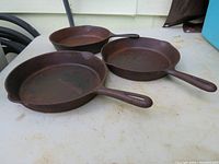 Three rusted cast iron skillets on table surface, two with handles facing right, one with handle facing left