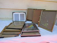 Photo showing a lot of 10 vintage metal picture frames in 8x10 inch size with glass and backing. Frames are stacked in piles and standing.