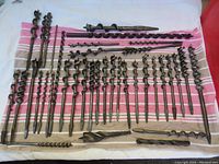 Overview of 38 wood auger bits laid out on towel showing various sizes and lengths