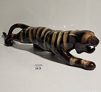 Side view of elongated panther figurine with glossy striped glaze in brown and cream hues.
